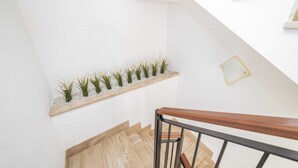 Una escalera con barandilla de madera, paredes blancas y un estante con plantas.