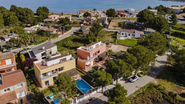 Vista aérea de una zona residencial costera con casas, piscina y vistas al mar y las montañas al fondo.