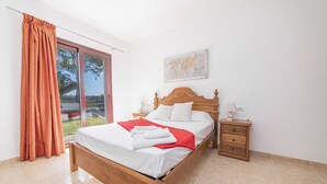 Una cama bien hecha con sábanas blancas y un plaid rojo, una mesita de noche de madera con una lámpara y un mapa mundial en la pared.