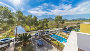 Zona de piscina con vista a un lago y montañas, rodeada de árboles y una valla.