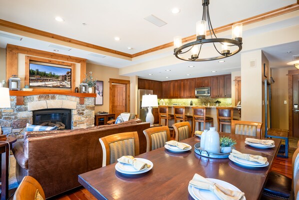 A dining area with a wooden table set for four, a stone fireplace, and wooden cabinetry.