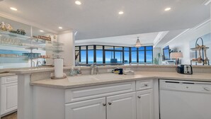 A modern kitchen with a large window overlooking the ocean, a built-in dishwasher, and a countertop with various kitchen items. - New to the Rental Market, Newly Owner, Newly Renovated!!! (Orange Beach)