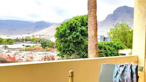 Un balcone con un tavolo, due bicchieri da vino e una bottiglia di champagne. Sullo sfondo, montagne, alberi e vista su un paese.