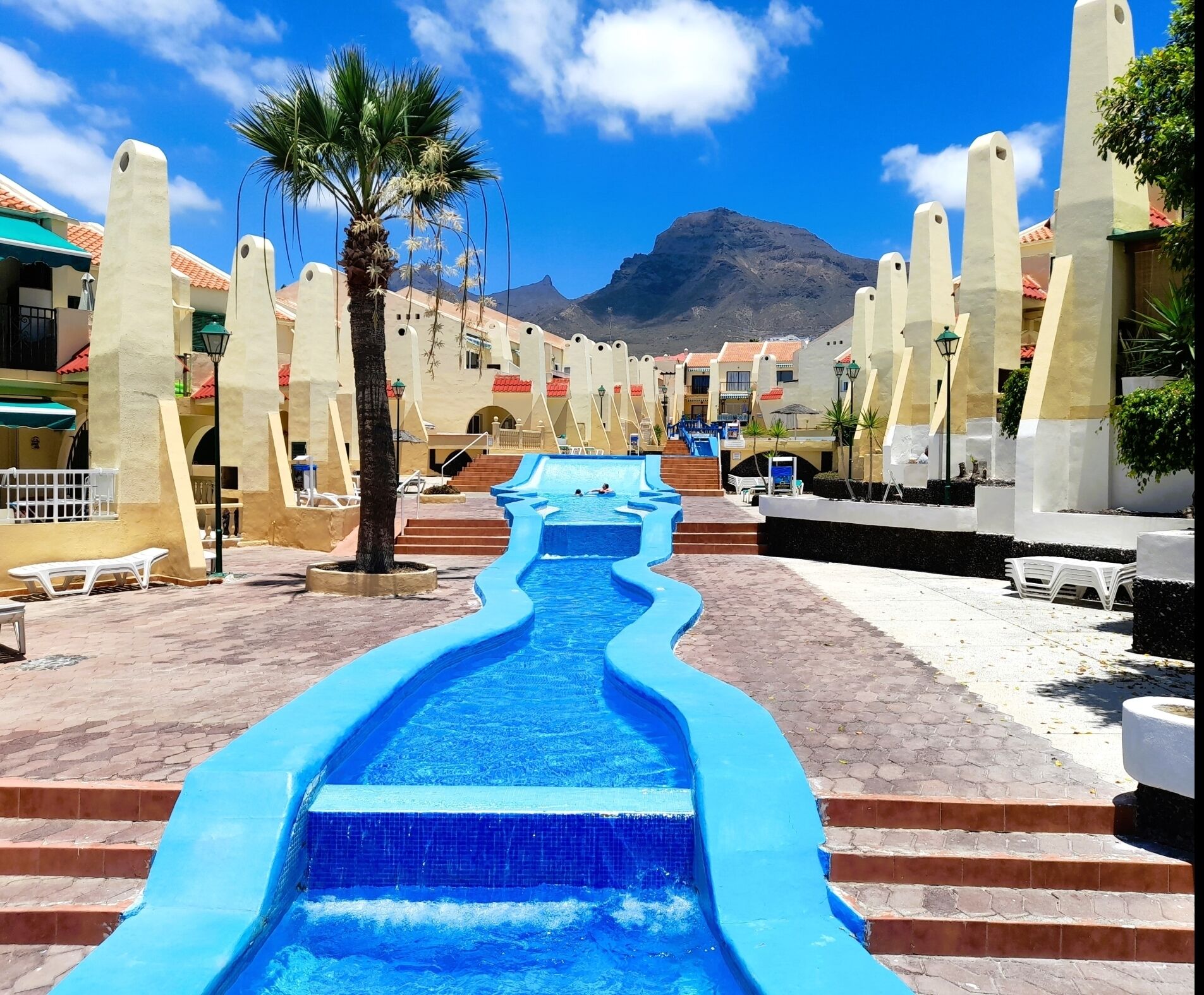A pool area with a blue water slide, palm trees, and steps leading to a pool.