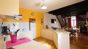 Une cuisine dotée d’un îlot central, un coin repas avec des chaises en bois, un escalier et une horloge au mur.