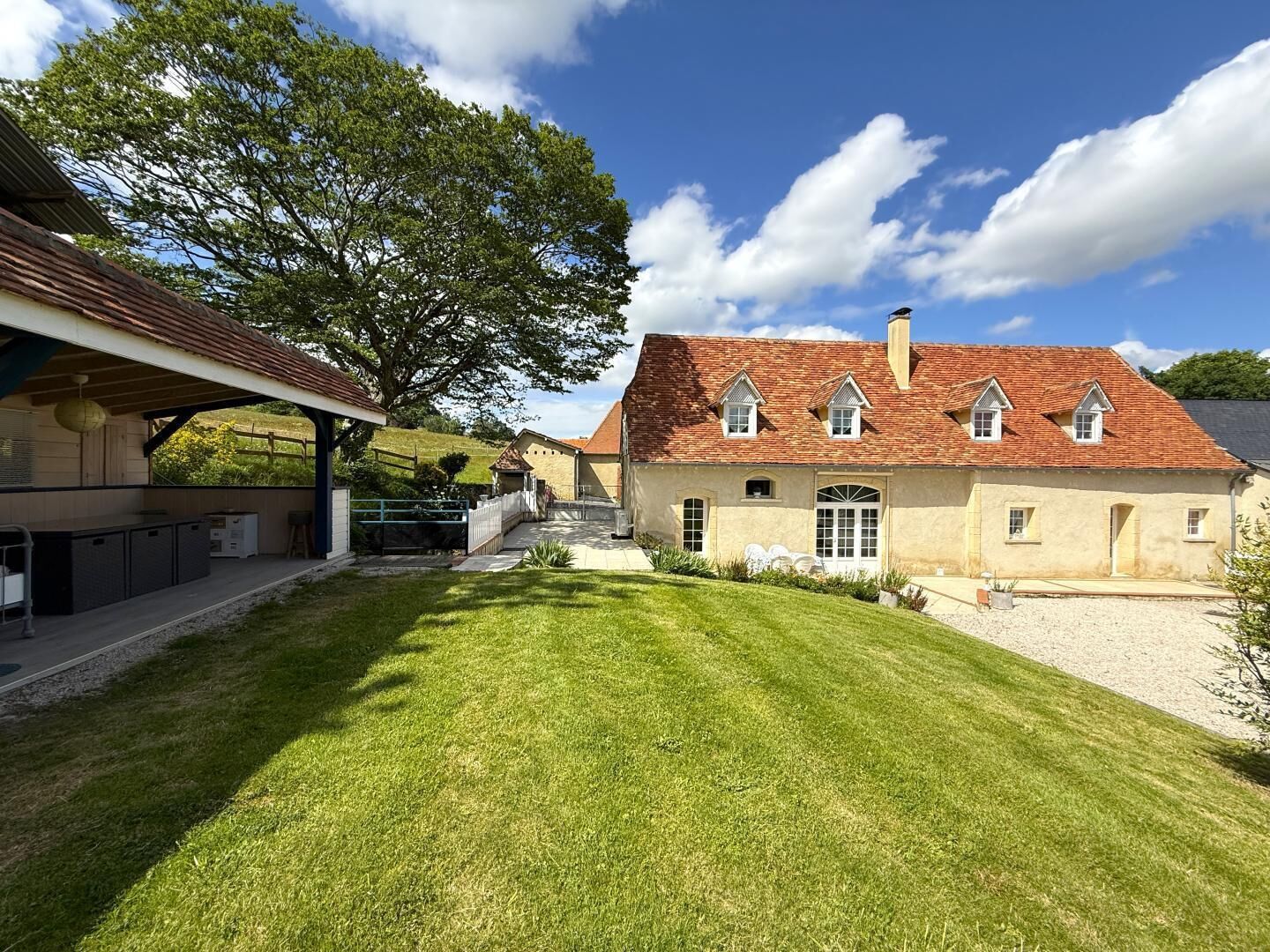 A house with a red-tiled roof, a covered outdoor area with a grill, and a well-maintained lawn.