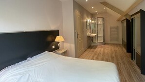 Una habitación de hotel moderna con una cama grande, una mesita de noche con lámpara, zona de ducha y vestidor.