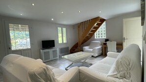 Una sala de estar moderna con muebles blancos, un televisor y una escalera que sube a un nivel superior.