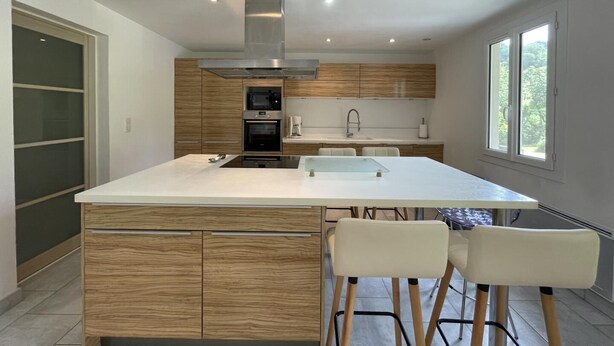 Una cocina moderna con una isla central, horno integrado, microondas y extractor de acero inoxidable.