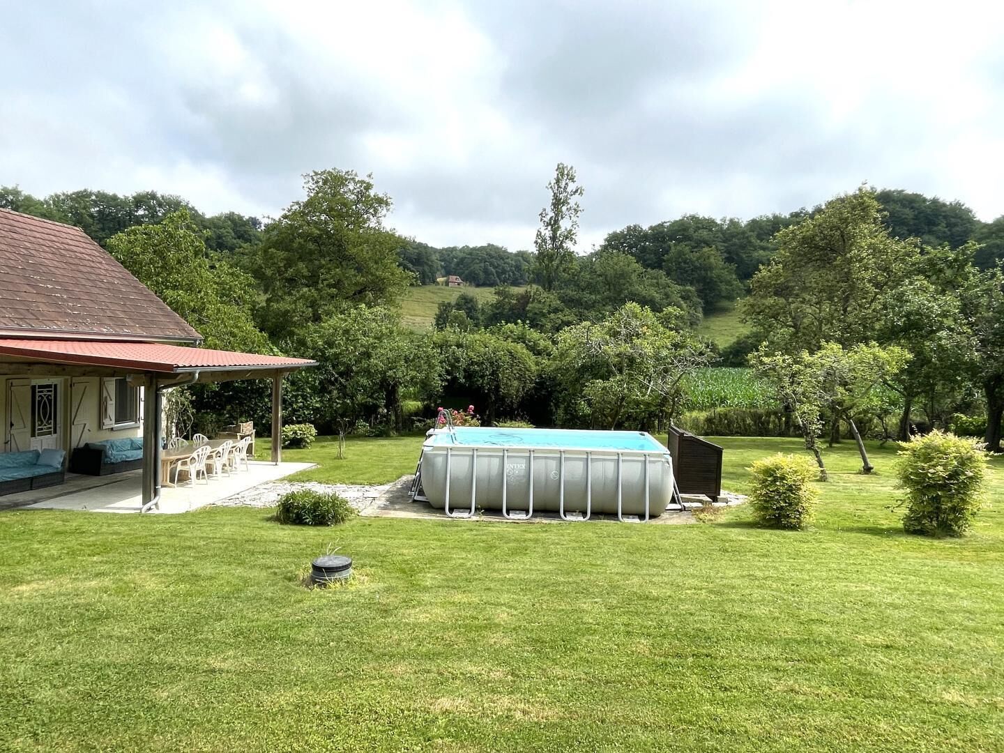 A house with a covered patio, a swimming pool, and a well-maintained lawn.