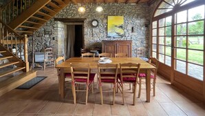 Een eethoek met een houten tafel en stoelen, een stenen muur, een trap en grote ramen.
