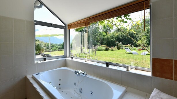 A bathroom with a large bathtub, a window with a view of a garden and mountains.