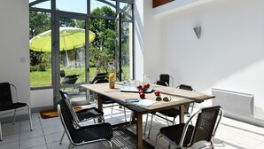 A modern dining area with a glass-enclosed patio, a wooden table, black chairs, and a yellow umbrella.