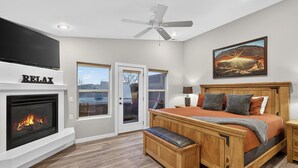 Une chambre à coucher avec une cheminée, un lit, un banc, un ventilateur de plafond et un tableau.