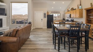 Une cuisine moderne avec des meubles en bois, une table à manger avec des chaises, un four encastré et une grande fenêtre offrant une vue sur l’extérieur.