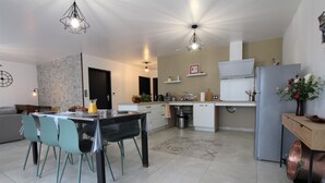 A modern kitchen with a dining area, featuring a stone wall, a refrigerator, and a coffee machine. - BARRANDEIA - JUXUE - Gîte (JUXUE)