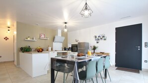 A modern kitchen with a dining area, featuring a central island, a black door, and a hanging light fixture. - BARRANDEIA - JUXUE - Gîte (JUXUE)