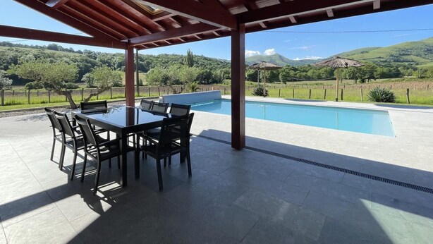 A covered outdoor area with a pool, a table with chairs, and a view of a hilly landscape. - BORDAZARRIA - JUXUE - Gîte (JUXUE)