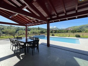 A covered outdoor area with a pool, a table with chairs, and a view of a hilly landscape. - BORDAZARRIA - JUXUE - Vacation Home (JUXUE)
