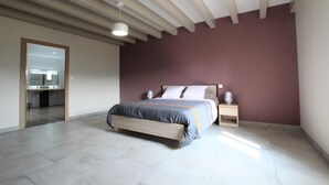 A modern bedroom with a large bed, a nightstand, a bedside lamp, and a bathroom visible through an open door. - BORDAZARRIA - JUXUE - Gîte (JUXUE)