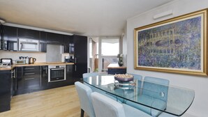 A modern kitchen with dark cabinetry, a glass dining table, and a large painting on the wall. - Wonderful Chelsea Flat, 2 Bedrooms, 2 Bathrooms (London)