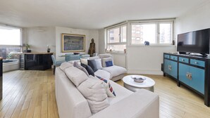 A modern living room with a sectional sofa, a coffee table, a TV, and a kitchen area with a counter and cabinets. - Wonderful Chelsea Flat, 2 Bedrooms, 2 Bathrooms (London)