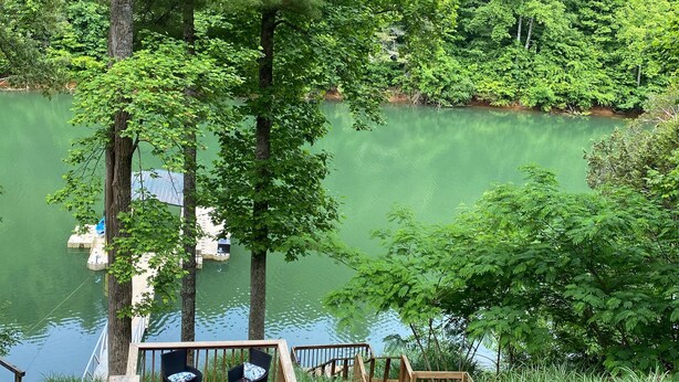 Una terraza de madera con mobiliario exterior con vistas a un lago tranquilo rodeado de abundante vegetación.