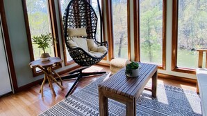 Una habitación con ventanas amplias, un sillón colgante, una mesita y una alfombra.