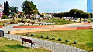 A park with a paved walkway, benches, and trimmed hedges. - New apartment Marin Punta-Umag near the sea (Umag)