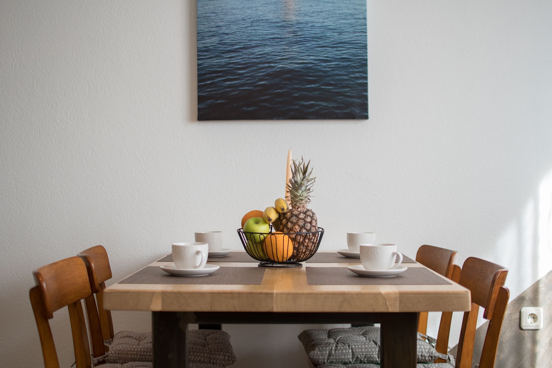 Ett matbord med en fruktskål, vita koppar och utsikt över vattnet.