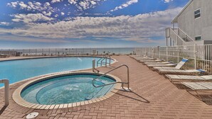 Ein Swimmingpool mit Whirlpool, umgeben von Liegestühlen und einer gepflasterten Terrasse, unter blauem Himmel.