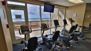 Ein Fitnessstudio mit Cardiogeräten und einem großen Fenster mit Blick auf den Strand.