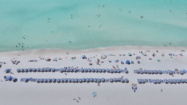 Eine Luftaufnahme eines Strandes mit Reihen von Sonnenschirmen und Menschen.
