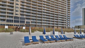 Ein Hotel direkt am Strand mit mehreren Etagen, einem Sandstrand mit blauen Liegestühlen und Sonnenschirmen.