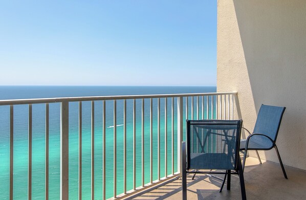 A balcony with a view of the ocean, a chair, and a wall.