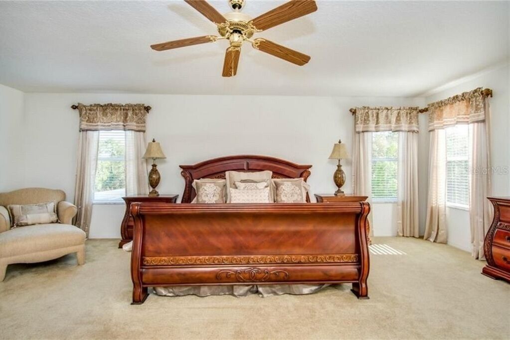 A bedroom with a large wooden bed, two bedside lamps, a ceiling fan, and a window with curtains.