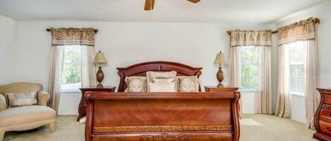 A bedroom with a large wooden bed, two bedside lamps, a ceiling fan, and a window with curtains.