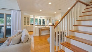 A spacious living room with a wooden staircase, a kitchen area with large windows, and a dining area. - Located Across From Beach in Seaside, Wrap-Around Porches + 2 Adult Bikes! (Santa Rosa Beach)