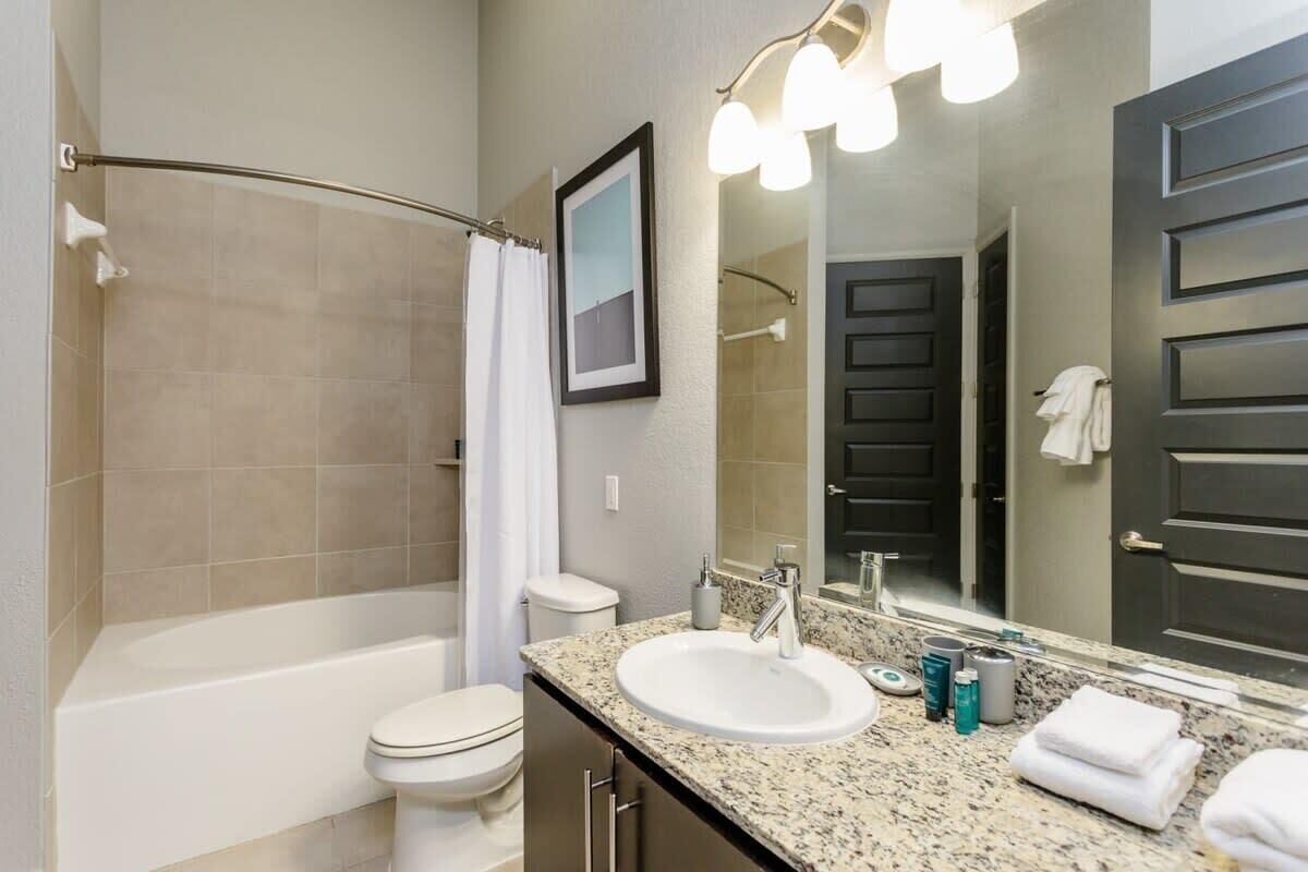 A bathroom with a bathtub, toilet, sink, and a large mirror.