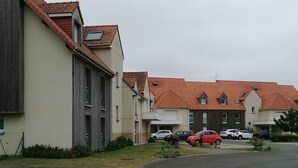 A row of residential buildings with red-tiled roofs and a parking lot in front. - Studio Cosy au Clos Fleuri 2 Personnes (Berck)