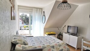 A bedroom with a bed, a desk, a chair, a TV, and a balcony with curtains. - Studio Cosy au Clos Fleuri 2 Personnes (Berck)