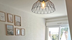 A living room with a grey sofa, yellow cushions, a white table with a vase, and framed pictures on the wall. - Studio Cosy au Clos Fleuri 2 Personnes (Berck)