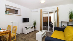 Un salon moderne doté d’un téléviseur à écran plat, de meubles en bois, d’un canapé et d’une porte-fenêtre coulissante donnant sur un coin repas.