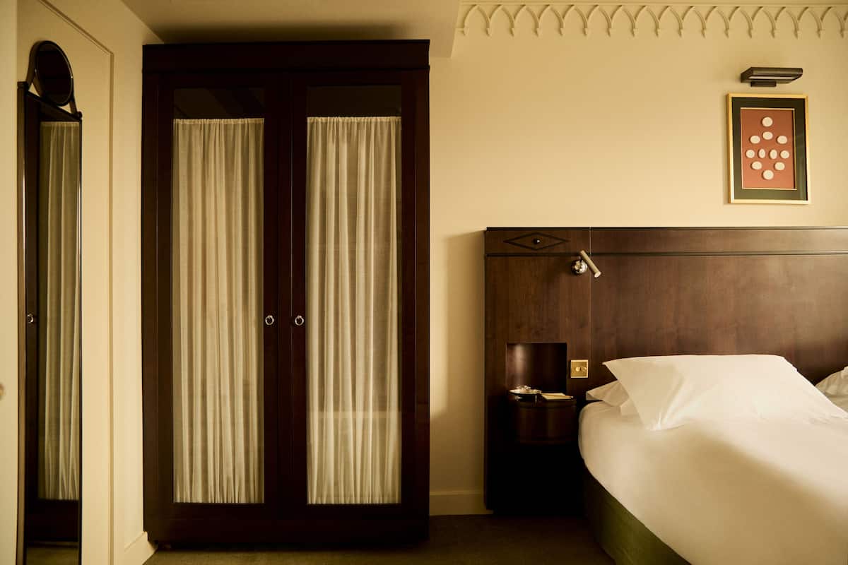 A hotel room with a wooden headboard bed, a nightstand with a lamp, and a large mirror on the door.