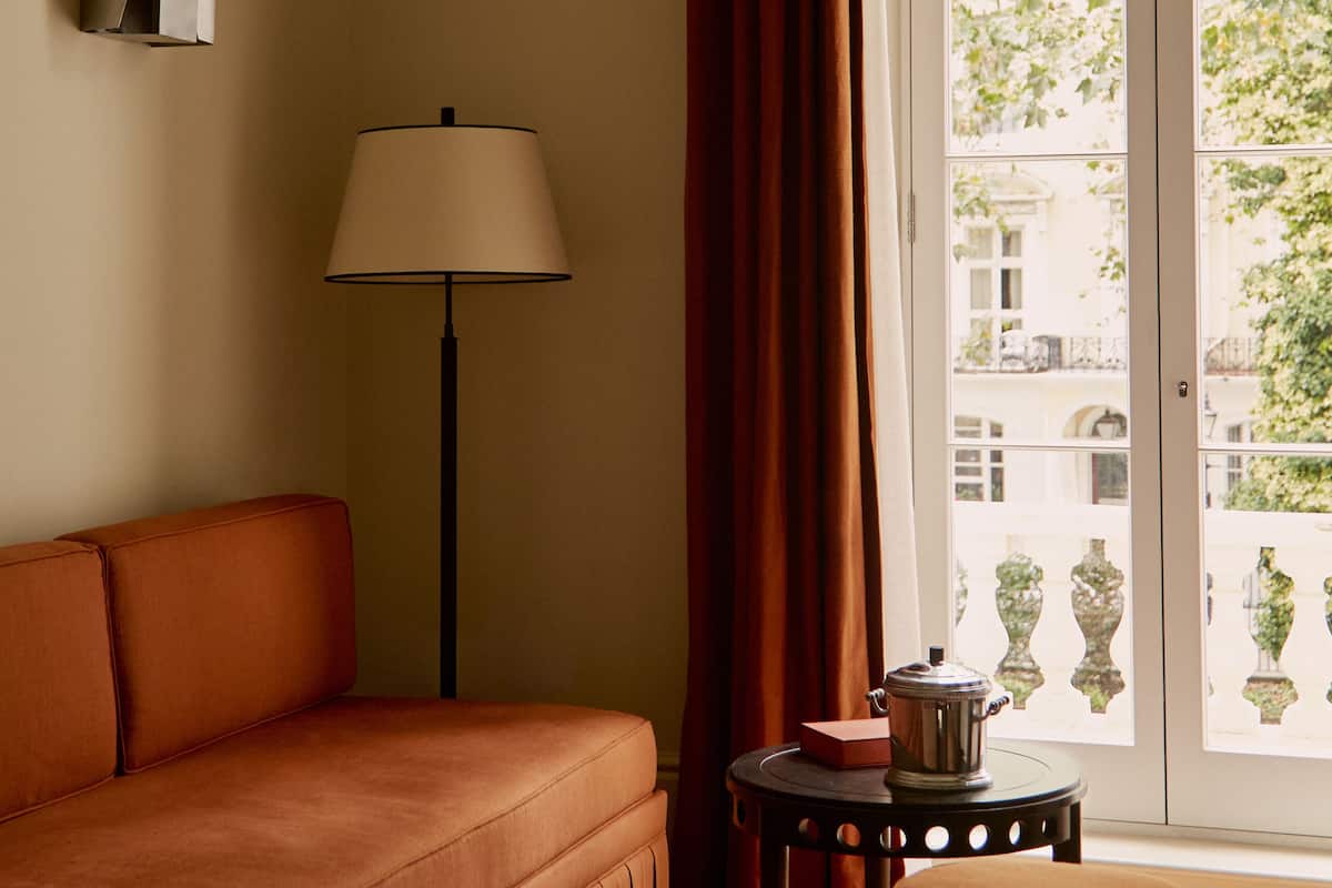 A room with a sofa, a lamp, a small table with a pot, and a view through a window.