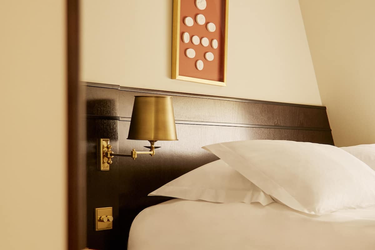 A neatly made bed with white linens, a wooden headboard, and a bedside lamp.