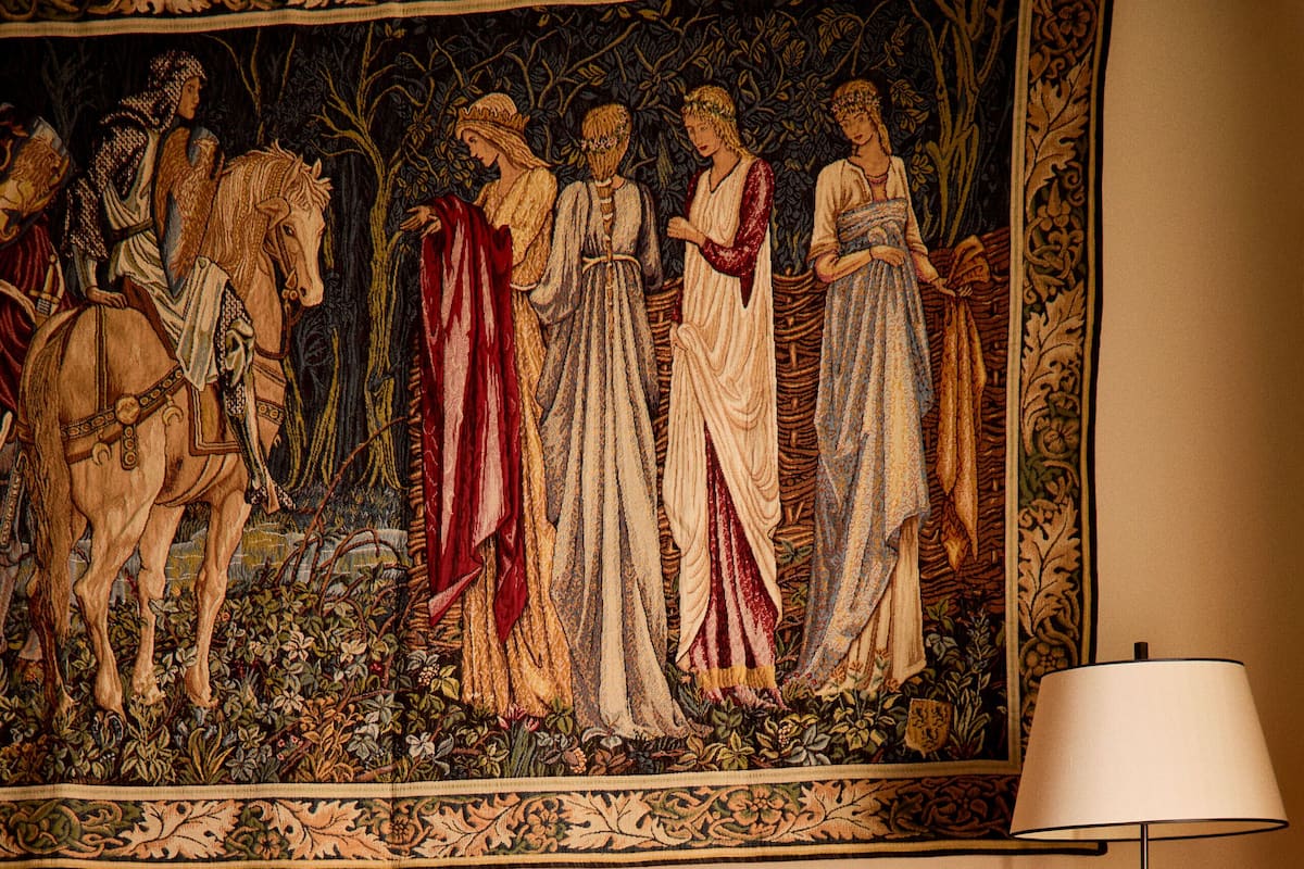 A room with a large tapestry, a sofa, a lamp, and a patterned rug.
