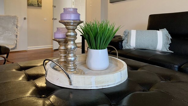 A living room with a black leather sofa, a white vase with green plants, and a decorative tray with purple candles. - The Gorge View Villa-with Yard & Parking (Niagara Falls)