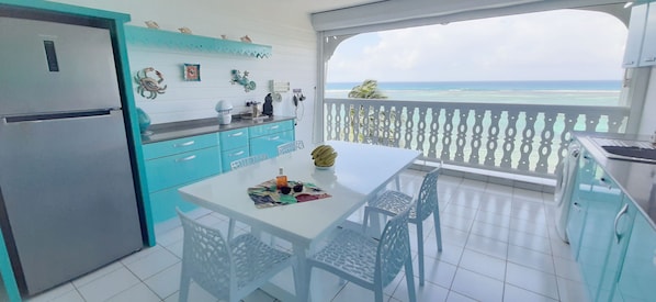 A kitchen with a refrigerator, a dining table with chairs, and a view of the ocean. - "Le Vanille", Résidence Savannah Face à la Mer (Saint-François)