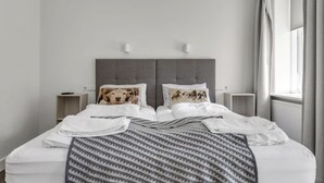 A neatly made bed with a patterned blanket, two bedside tables with lamps, and a window with curtains.